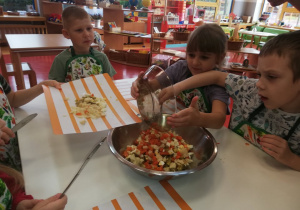 chłopiec z dziewczynką wrzucają do miski pokrojone warzywa